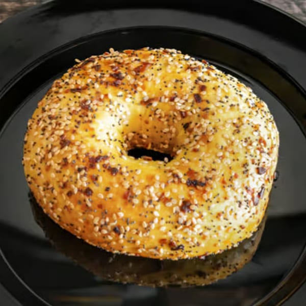 A Rocket Bagels Deli & Catering everything bagel, topped with poppy and sesame seeds, on a black plate.
