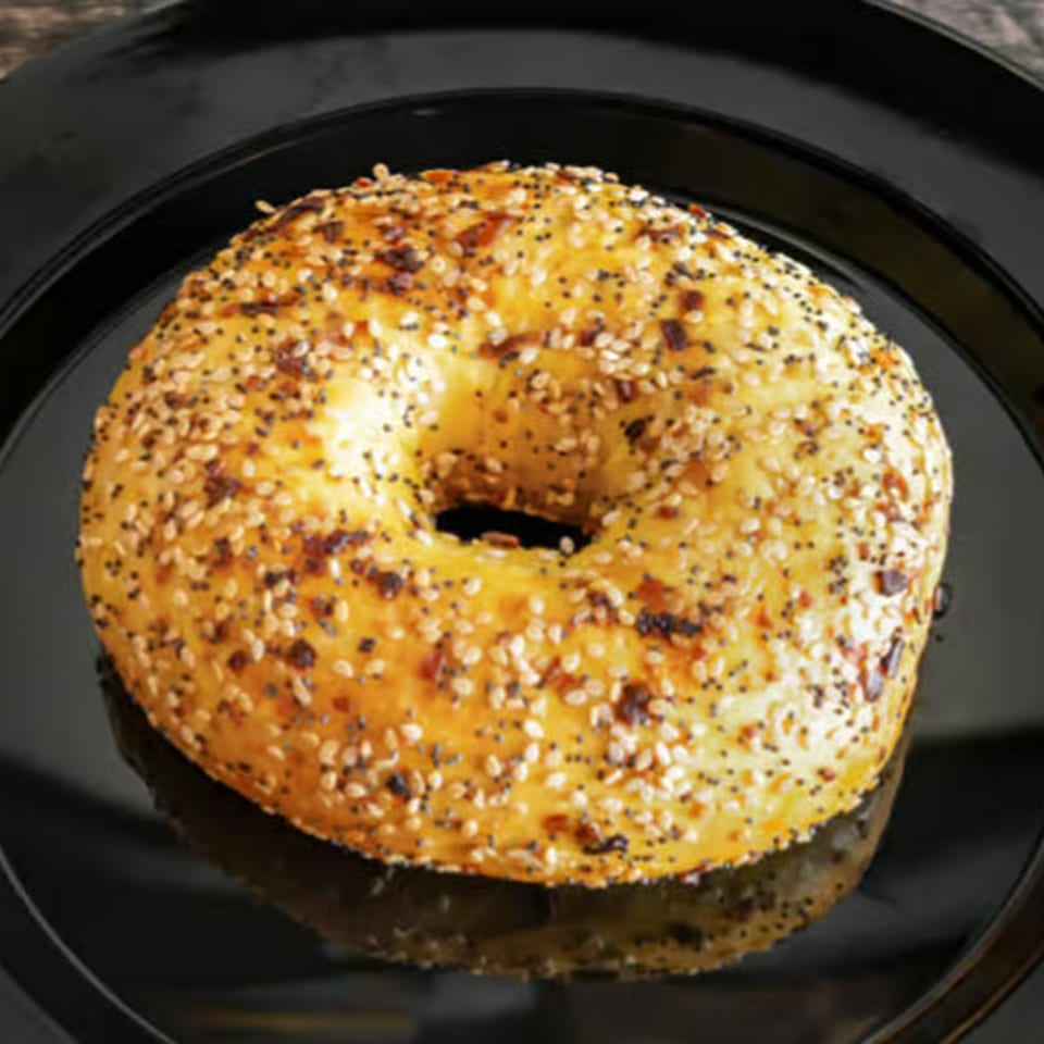 A Rocket Bagels Deli & Catering everything bagel, topped with poppy and sesame seeds, on a black plate.
