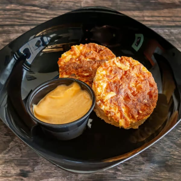 Two golden-brown bagel bombs with a side of creamy orange dipping sauce on a black plate.