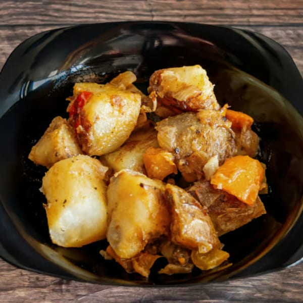 Close-up of a black bowl filled with roasted potatoes, carrots, and meat on a wooden table.