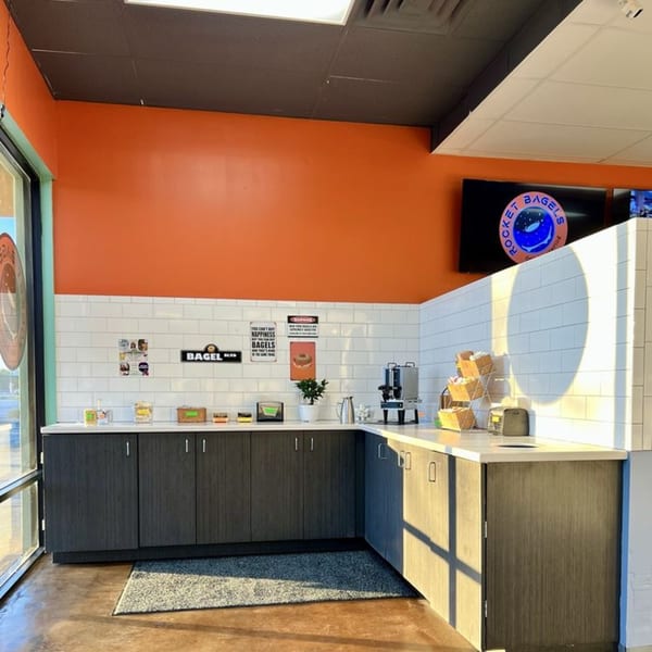 Interior of Rocket Bagels with orange walls, white subway tile, and a self-serve counter.