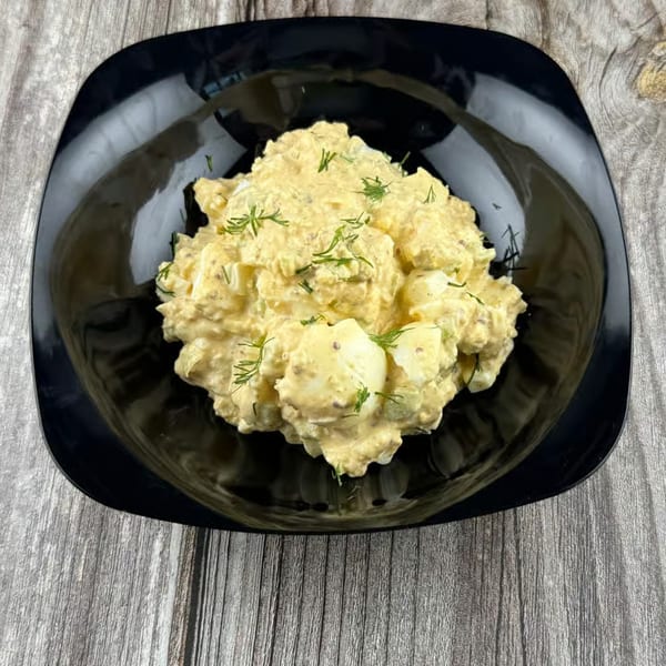 Creamy egg salad with fresh dill in a black bowl on a rustic wooden surface.