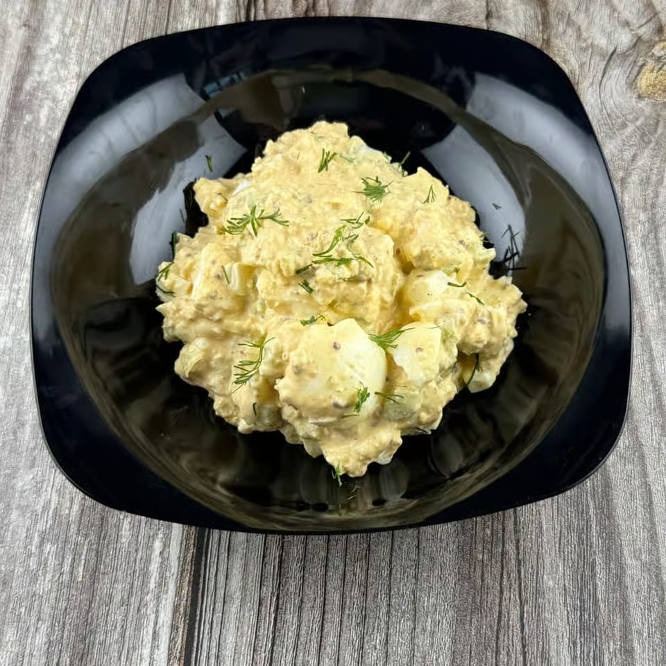Creamy egg salad with fresh dill in a black bowl on a rustic wooden surface.