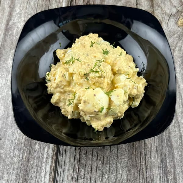 Creamy egg salad with fresh dill in a black square bowl on a rustic wooden surface.