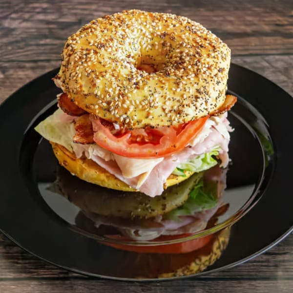 Everything bagel sandwich with turkey, bacon, lettuce, and tomato on a black plate.