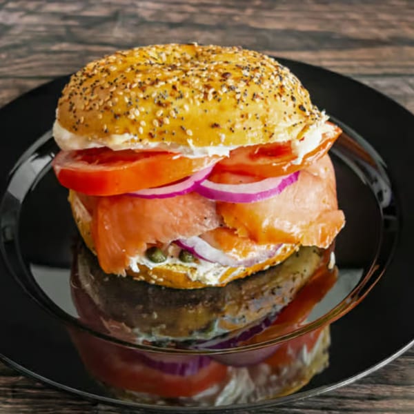 Everything bagel with lox, cream cheese, red onion, tomatoes, and capers on a black plate.