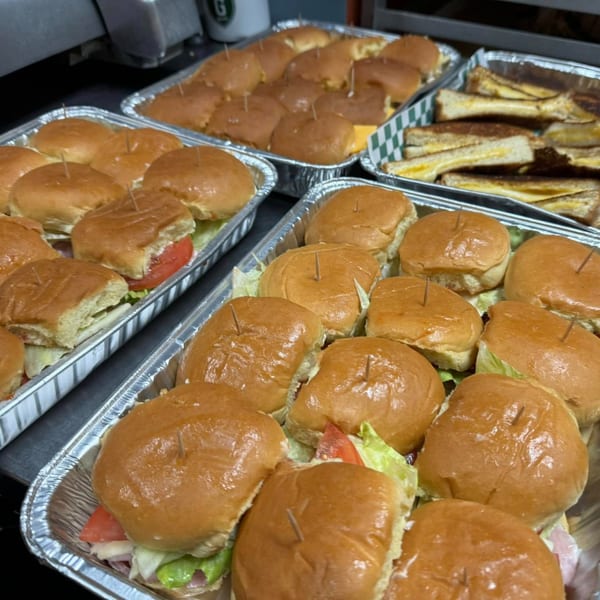 Multiple catering trays filled with mini sandwiches and grilled cheese triangles from Rocket Bagels.