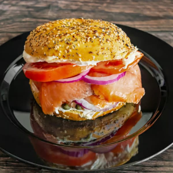 Everything bagel with lox, cream cheese, tomato, red onion, and capers on a black plate.