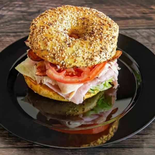Everything bagel sandwich with turkey, bacon, lettuce, and tomato on a black plate.