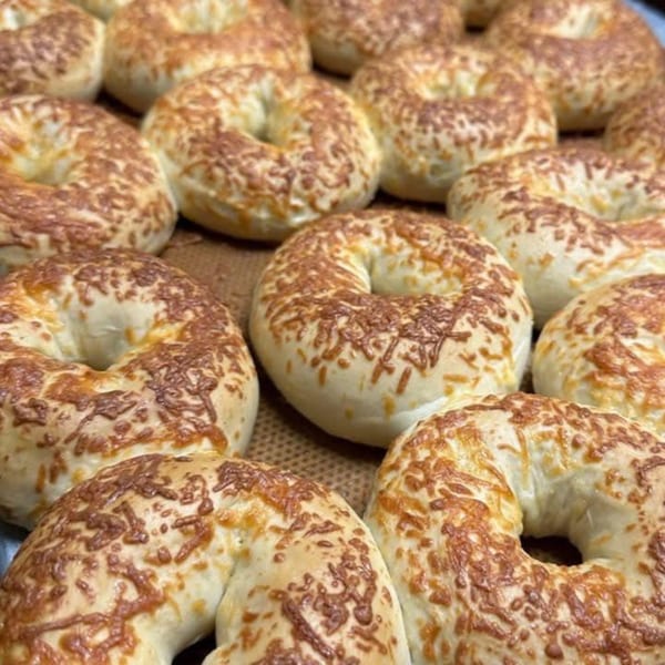 Close-up of many freshly baked Rocket Bagels Deli & Catering cheese bagels on a baking sheet.