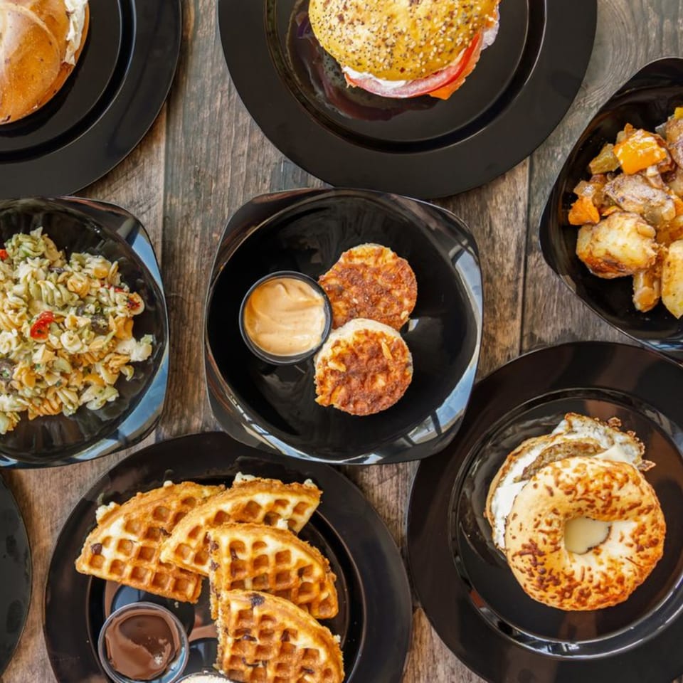 Overhead view of various Rocket Bagels Deli & Catering dishes, including bagels, waffles, and pasta salad.